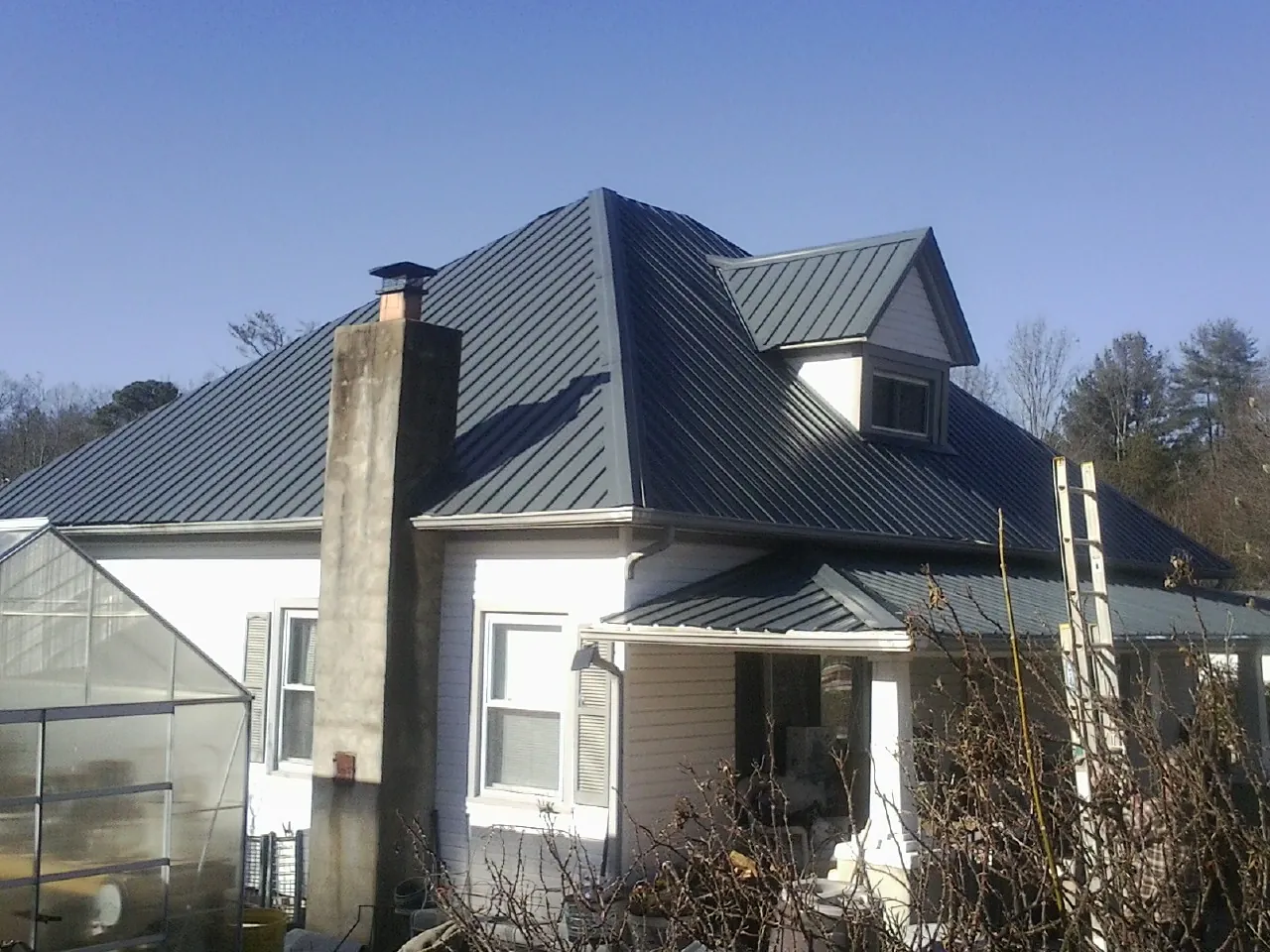 Dark blue standing seam metal roof on a white farmhouse with dormer — Slate & Tile Roof Repair by Roofing Brothers in Dearborn Heights