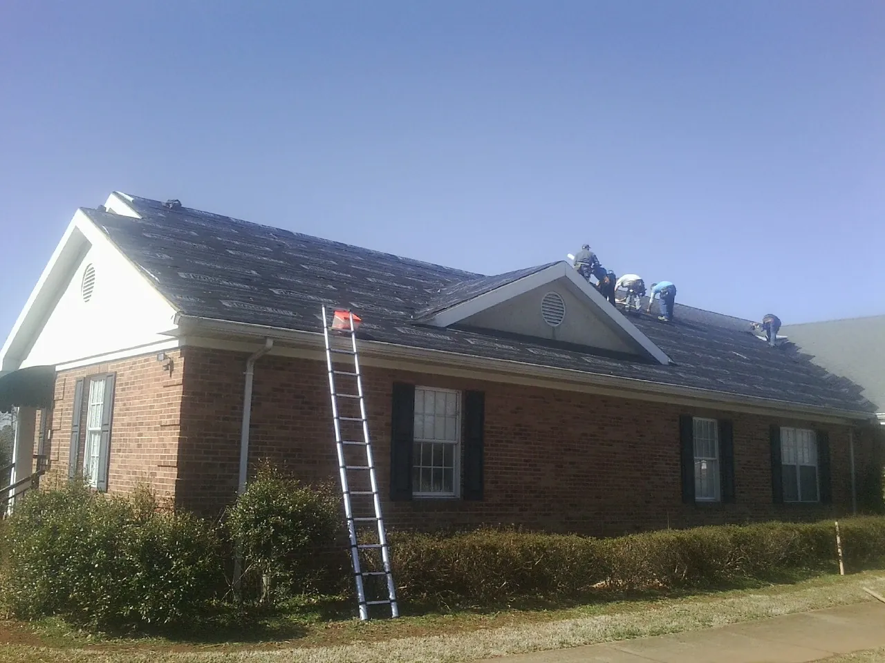 Crew tearing shingles off a brick ranch roof with a ladder set — Emergency Roof Repair work by our crew in Dearborn Heights
