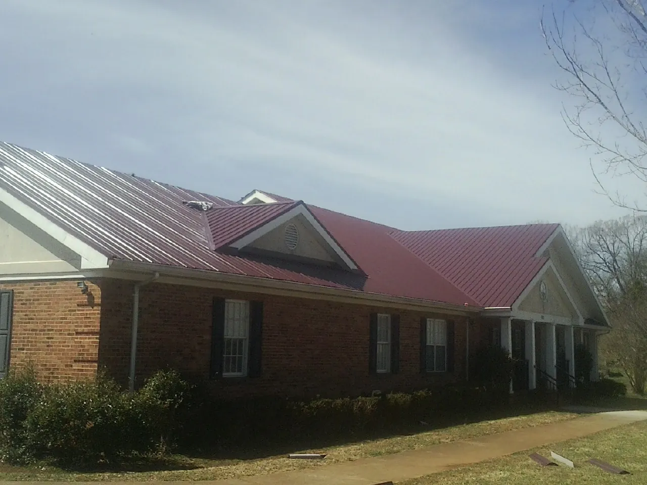 Red metal roof with gabled entries on a long brick building, from a Hail Damage Roof Repair job in Dearborn Heights