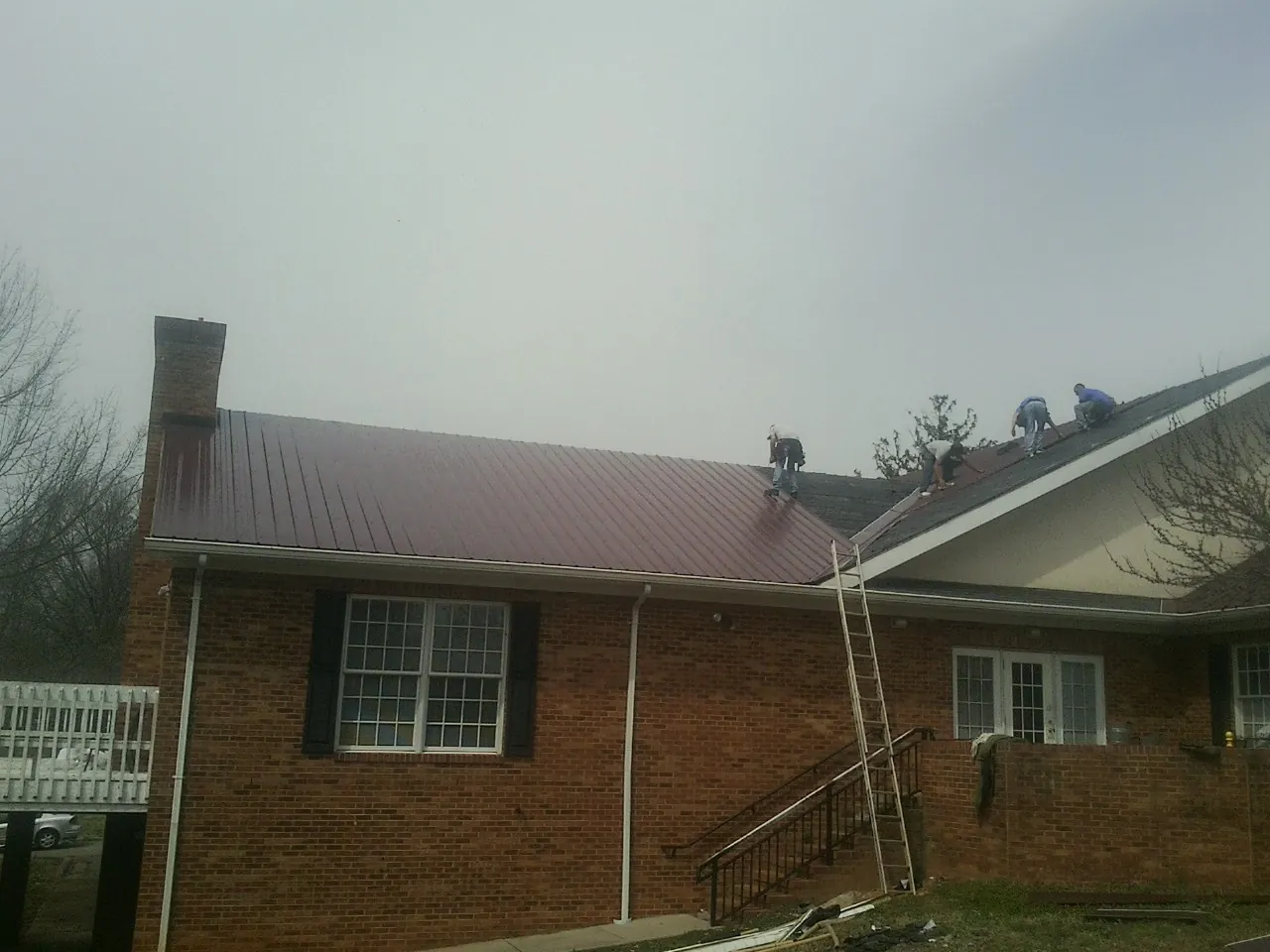Crew setting red metal roofing panels on a brick home in Dearborn Heights