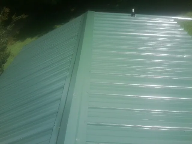 New green metal panels meeting at the ridge of a roof — Flat Roof Repair work by our crew in Dearborn Heights