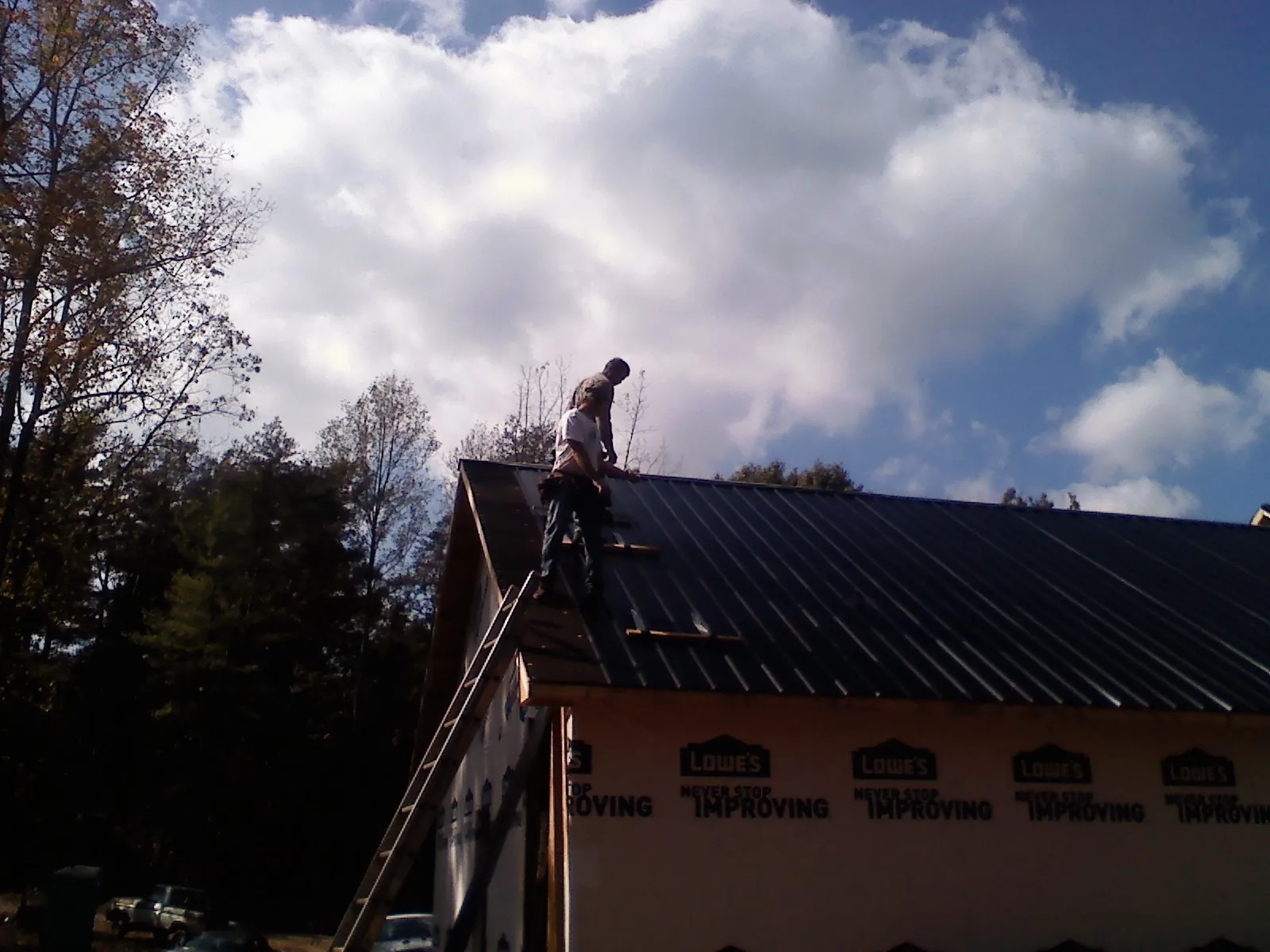 Roofer fastening dark metal panels high against a cloudy sky, from a Roof Inspection job in Dearborn Heights