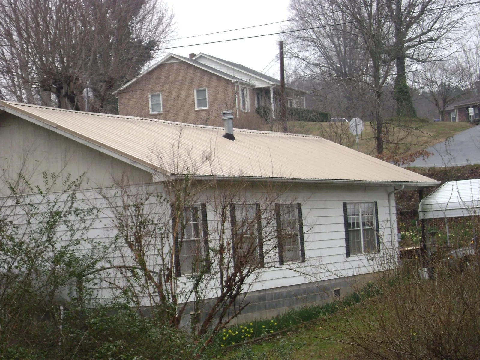 Tan metal roof on a white sided house set into a hillside — Commercial Roofing by Roofing Brothers in Dearborn Heights